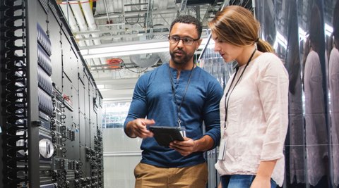 A male and female IT Technician in a server room checking out wired equipment.